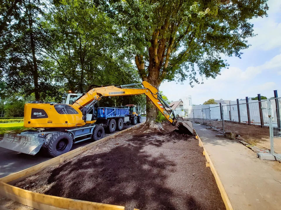 Er wordt grond in een bak verdeeld met een graafmachine